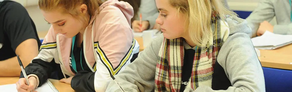 Students writing at a desk in a classroom